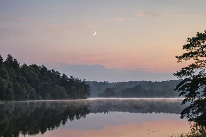 Der Mond am Abendhimmel über einer Landschaft — Beitragsbild zu „Was bedeutet der Neumond in der Natur und Spiritualität?“